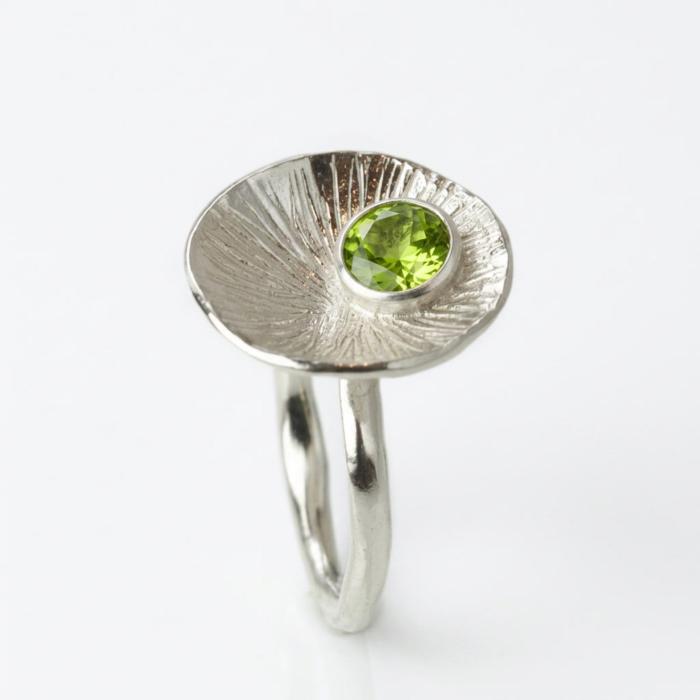 Handgefertigter Damenring aus Silber mit grünem facettiertem Peridot in runder Fassung auf strukturierter Scheibe und gehämmerter Ringschiene.